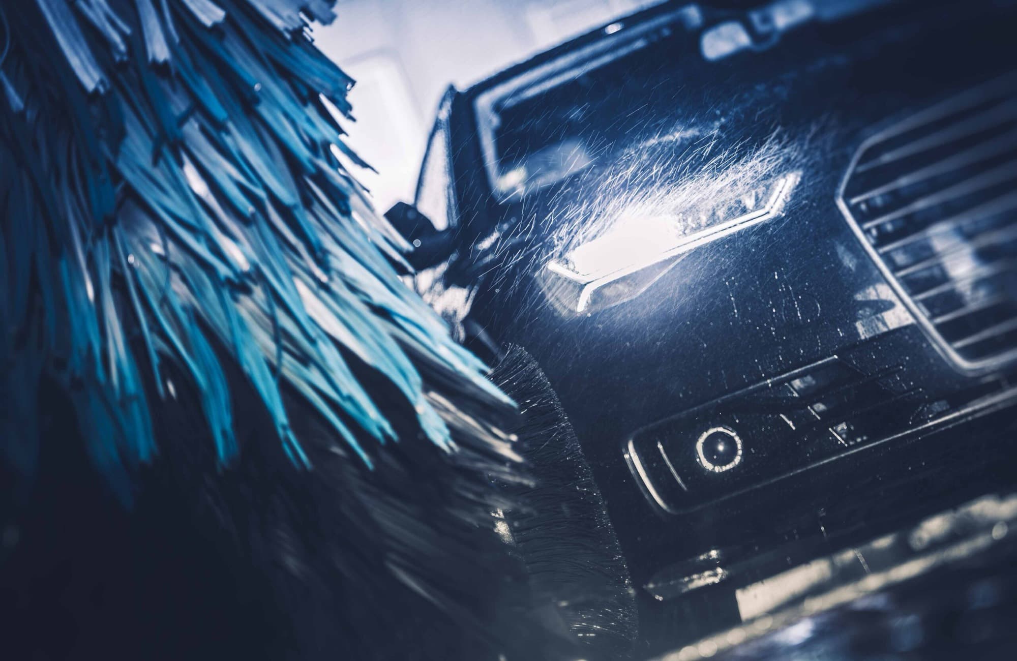 A car moving through an automatic wash as foaming brushes and water spray clean it